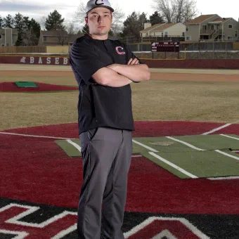 Baseball player standing on the field with arms crossed, wearing a cap and uniform.